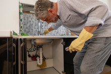 Mature Man Repairing Faucet In Kitchen At Home