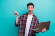 © deagreez - Photo of positive excited guy wear checkered shirt chatting modern device pointing empty space isolated blue teal color background