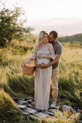 Beautiful young pregnant couple spending time together in outdoor at sunset. The concept of expecting a baby, parenthood.