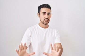 Wall Mural - Handsome hispanic man standing over white background afraid and terrified with fear expression stop gesture with hands, shouting in shock. panic concept.