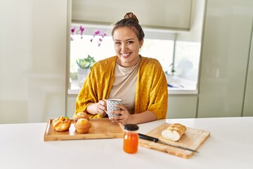 Poster - Young beautiful hispanic woman having breakfast drinking coffee at the kitchen