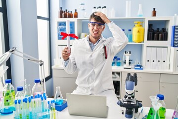 Sticker - Young hispanic man working at scientist laboratory holding diploma stressed and frustrated with hand on head, surprised and angry face