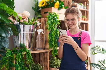 Poster - Young blonde woman florist smiling confident using smartphone at flower shop