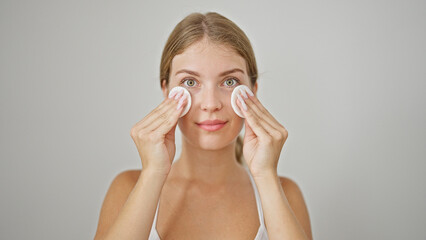 Wall Mural - Young blonde woman cleaning face with cotton pad over isolated white background