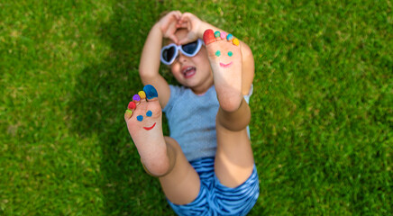 Child feet drawing smile in the park on the grass. Selective focus.