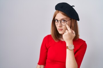 Sticker - Young redhead woman standing wearing glasses and beret pointing to the eye watching you gesture, suspicious expression