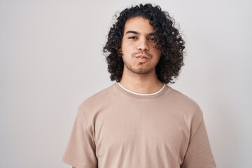 Sticker - Hispanic man with curly hair standing over white background puffing cheeks with funny face. mouth inflated with air, crazy expression.