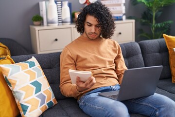 Poster - Young latin man using laptop reading notebook at home