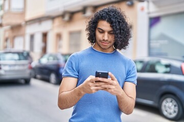 Wall Mural - Young latin man using smartphone with serious expression at street