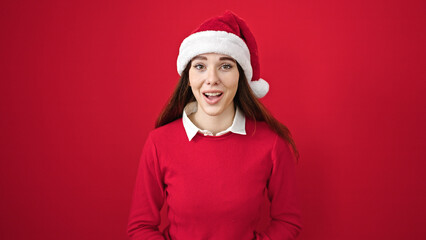 Poster - Young hispanic woman wearing christmas hat with surprise expression over isolated red background