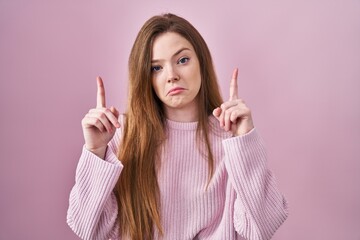 Canvas Print - Young caucasian woman standing over pink background pointing up looking sad and upset, indicating direction with fingers, unhappy and depressed.