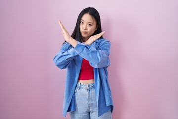 Poster - Young asian woman standing over pink background rejection expression crossing arms doing negative sign, angry face