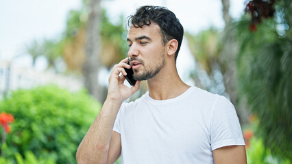 Wall Mural - Young hispanic man talking on smartphone with serious expression at park