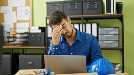 Young hispanic man architect using touchpad and laptop stressed at office