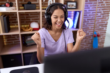 Wall Mural - Young african american woman streamer playing video game with winner expression at gaming room