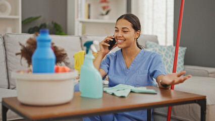 Canvas Print - African american woman professional cleaner cleaning table talking on smartphone at home