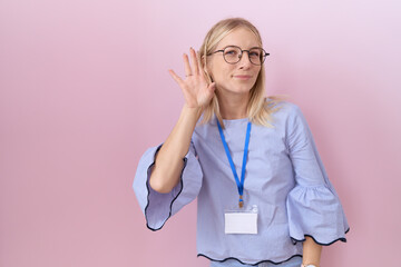 Poster - Young caucasian business woman wearing id card smiling with hand over ear listening an hearing to rumor or gossip. deafness concept.