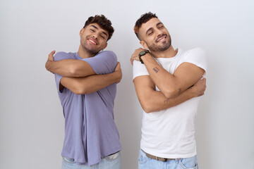 Poster - Homosexual gay couple standing over white background hugging oneself happy and positive, smiling confident. self love and self care