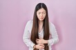© Krakenimages.com - Chinese young woman standing over pink background with hand on stomach because indigestion, painful illness feeling unwell. ache concept.