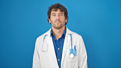 Canvas Print - Young hispanic man doctor standing with serious expression over isolated blue background