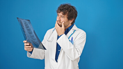 Canvas Print - Young hispanic man doctor looking xray over isolated blue background