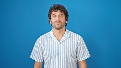 Poster - Young hispanic man standing with serious face over isolated blue background