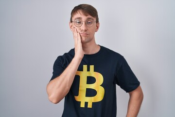 Poster - Caucasian blond man wearing bitcoin t shirt thinking looking tired and bored with depression problems with crossed arms.