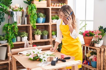 Sticker - Young blonde woman florist talking on smartphone writing on notebook at florist