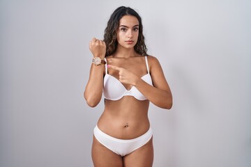 Sticker - Young hispanic woman wearing white lingerie in hurry pointing to watch time, impatience, looking at the camera with relaxed expression