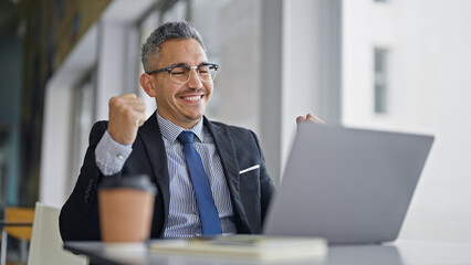 Poster - Young hispanic man business worker using laptop with winner gesture at office