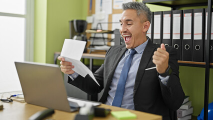 Wall Mural - Young hispanic man business worker reading letter celebrating at office