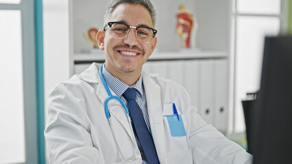 Poster - Young hispanic man doctor using computer wearing glasses at clinic