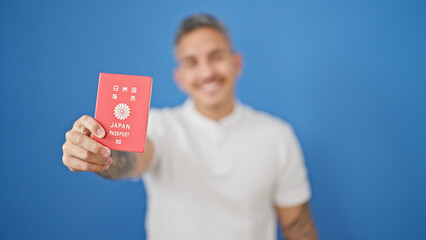 Canvas Print - Young hispanic man smiling confident holding japan passport over isolated blue background