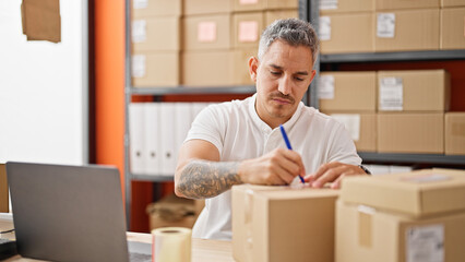 Wall Mural - Young hispanic man ecommerce business worker using laptop writing on package at office