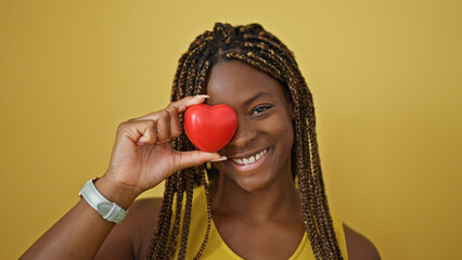 Poster - African american woman smiling confident holding heart over eye over isolated yellow background