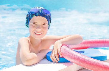 Healthy lifestyle. Active child (boy) in cap, sport goggles ready to learns professional swimming with pool board and swim noodles in swimming pool. Kid enjoying water.