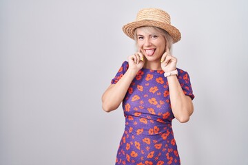 Sticker - Young caucasian woman wearing flowers dress and summer hat smiling pulling ears with fingers, funny gesture. audition problem