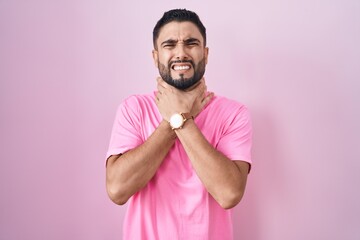 Poster - Hispanic young man standing over pink background shouting suffocate because painful strangle. health problem. asphyxiate and suicide concept.