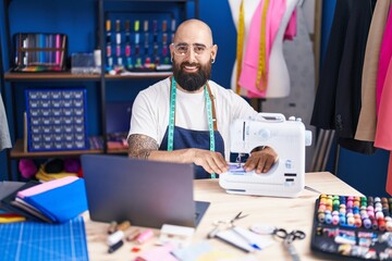 Poster - Young bald man tailor using sewing machine and laptop at clothing factory