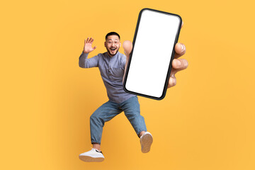 Wall Mural - Asian man holding large cellphone blank screen leaping in studio