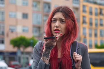 Wall Mural - young woman sending a voice or audio message with mobile phone on the street