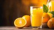 © Gautier Normand - Un verre rempli de jus d'orange frais, entouré de plusieurs oranges entières et d'une orange coupée en deux, sur une table en bois.
