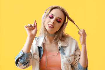 Wall Mural - Young woman in headphones chewing gum on yellow background