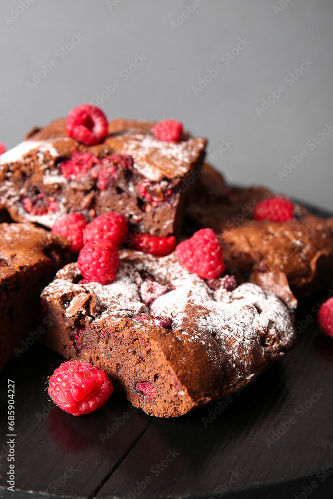 Board with pieces of raspberry chocolate brownie on grey background