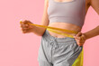 Beautiful young woman with measuring tape on pink background, closeup. Weight loss concept