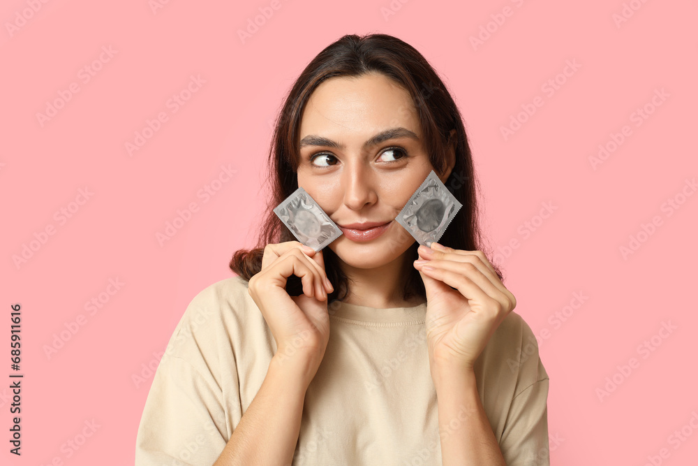 Thoughtful young woman with condoms on pink background. Safe sex concept