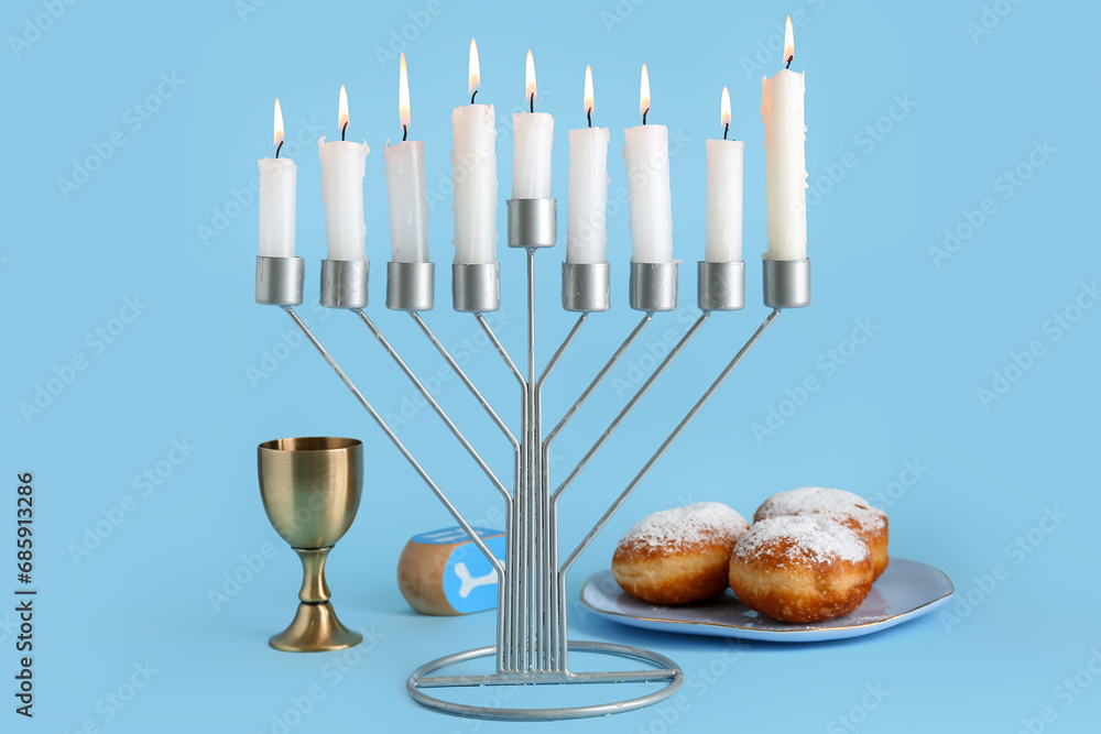 Menorah, donuts, cup and dreidel for Hanukkah celebration on color background