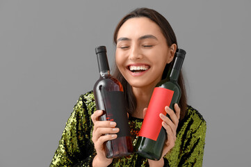 Sticker - Beautiful young woman with bottles of wine on grey background