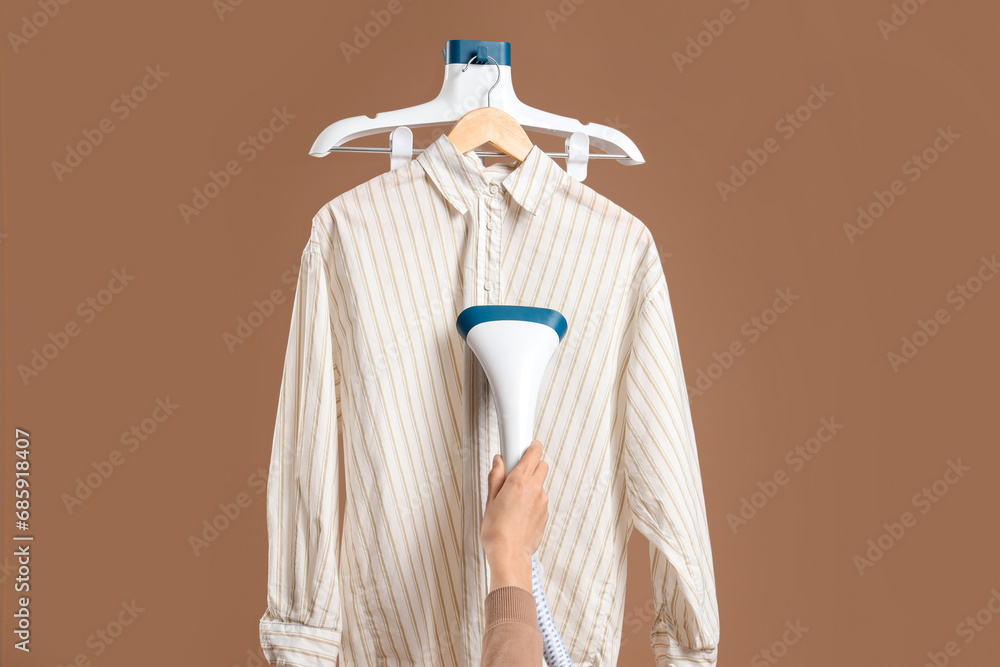 Woman steaming clothes with modern steamer on brown background