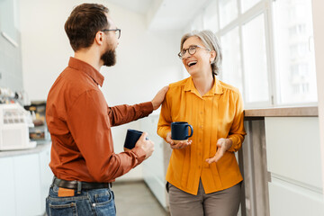 Wall Mural - Happy bearded man touching shoulder of business colleague while drinking coffee